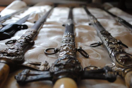 HD PC desktop wallpaper showing a close-up of man-made swords with ornate hilts laid out on a patterned fabric surface.