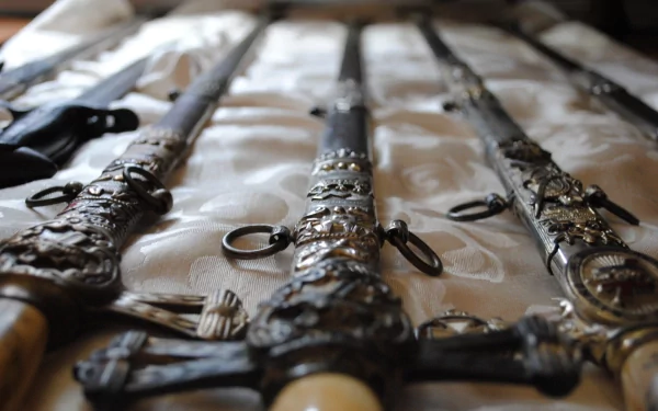 HD PC desktop wallpaper showing a close-up of man-made swords with ornate hilts laid out on a patterned fabric surface.