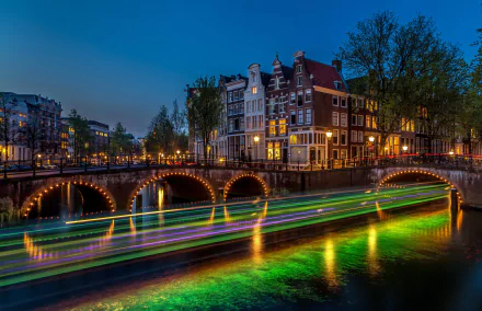 A vibrant night scene in Amsterdam featuring illuminated buildings and a bridge over a canal, with colorful lights reflecting on the water, captured in stunning 4K Ultra HD.