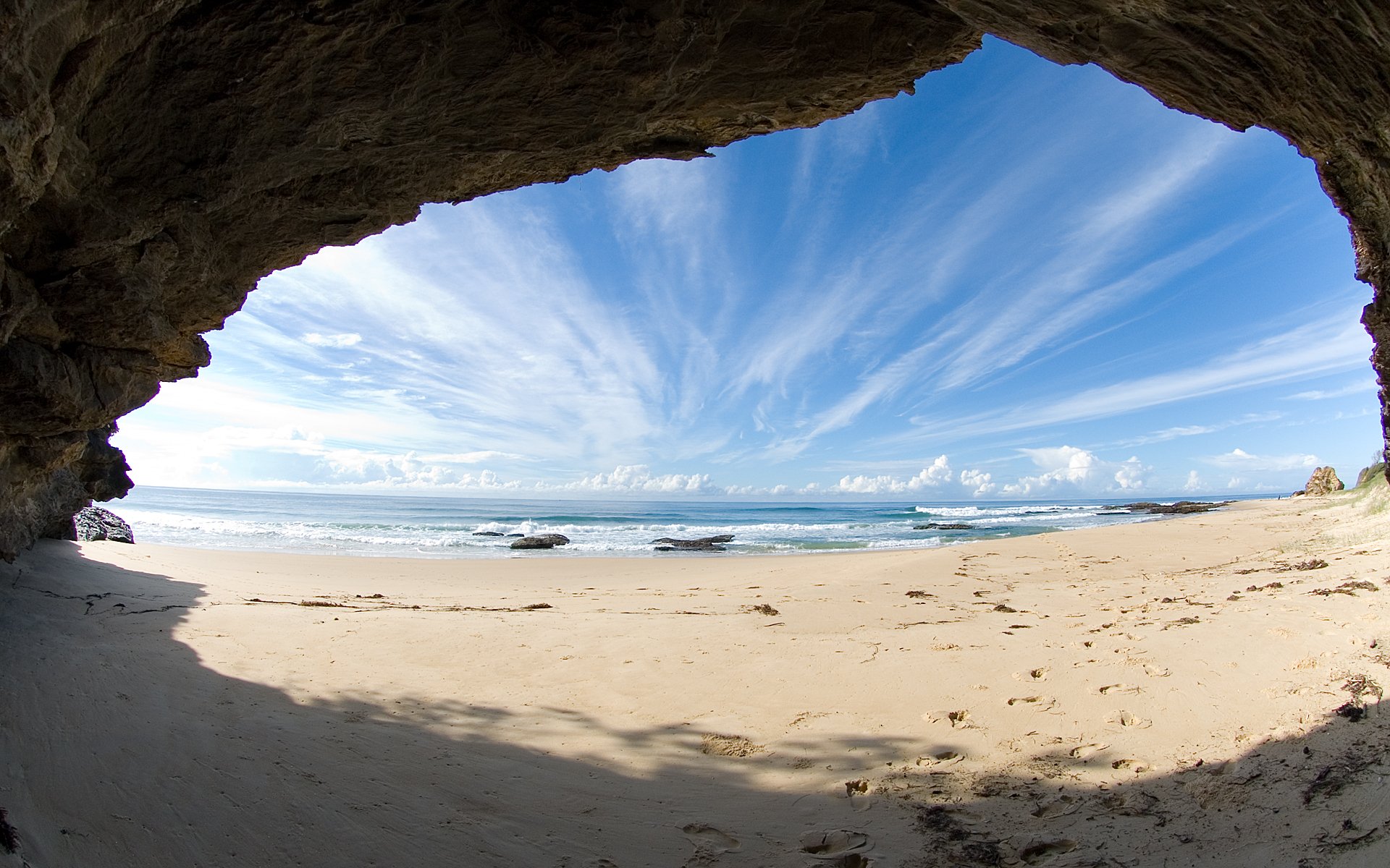 A breathtaking view of the beach framed by a rocky cave, showcasing the vast ocean under a vibrant sky. This HD wallpaper captures the beauty of nature's coastal landscape.