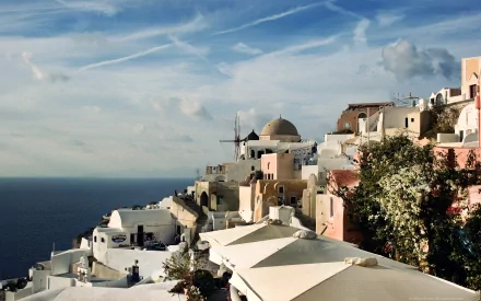 HD desktop wallpaper of a scenic coastal city with white and pastel buildings sprawled on a hillside, against a backdrop of the sea and a partly cloudy sky.