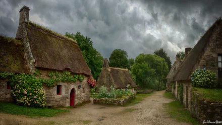 HD desktop wallpaper of a charming English cottage scene featuring man-made thatched roof houses under dramatic cloud-filled skies.