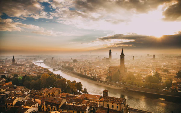 Foggy Verona cityscape at the horizon: a river winds through tiled houses and historic man-made buildings under warm light — HD PC desktop wallpaper and background