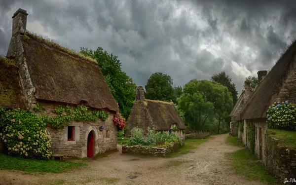 HD desktop wallpaper of a charming English cottage scene featuring man-made thatched roof houses under dramatic cloud-filled skies.