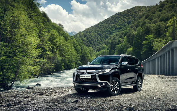 Black Mitsubishi Pajero SUV parked by a river with lush green hills and a cloudy sky in the background, captured in 4K Ultra HD for PC desktop wallpaper.