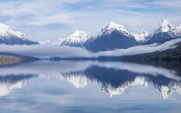 Panoramic view of Lake McDonald in Glacier National Park, Montana, USA. Snow-capped mountains and fog are reflected in the calm lake, creating a serene HD wallpaper and background.