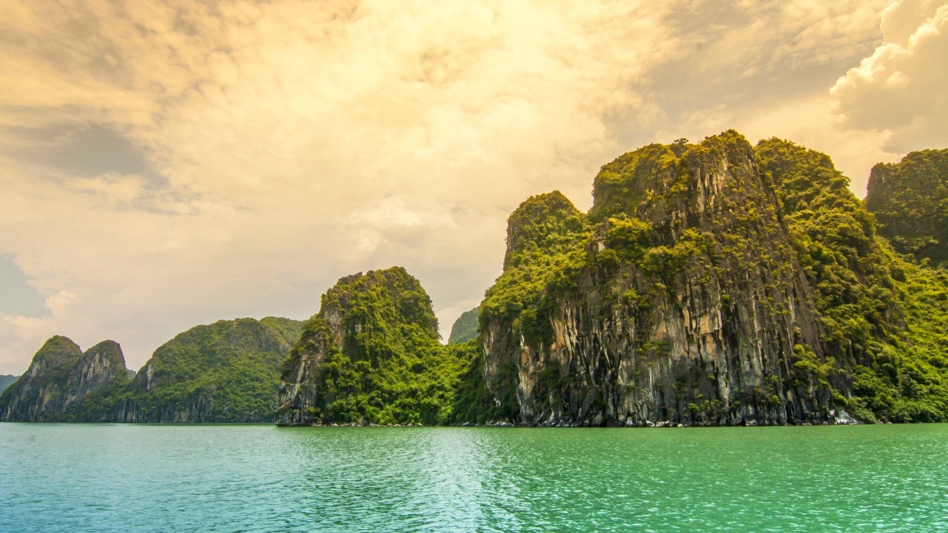HD desktop wallpaper showing a stunning coastline with towering green cliffs in Indonesia under a golden sky.