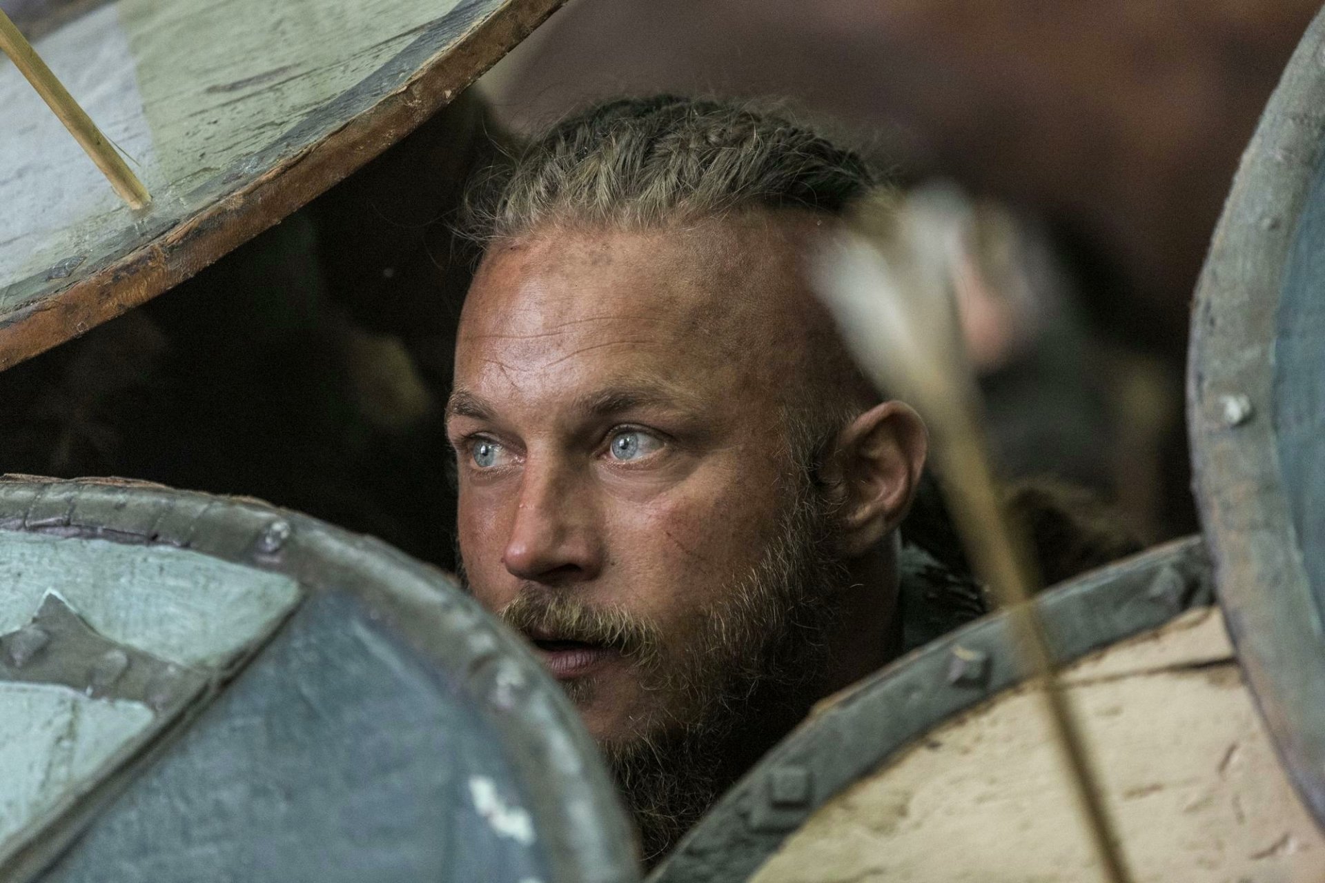 HD desktop wallpaper from the TV show Vikings (2013) featuring Ragnar Lothbrok peering through Viking shields in a tense moment.