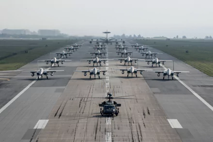 A striking 4K Ultra HD image featuring a Sikorsky HH-60 Pave Hawk helicopter in the foreground, with rows of McDonnell Douglas F-15 Eagle fighter jets lined up on a runway.