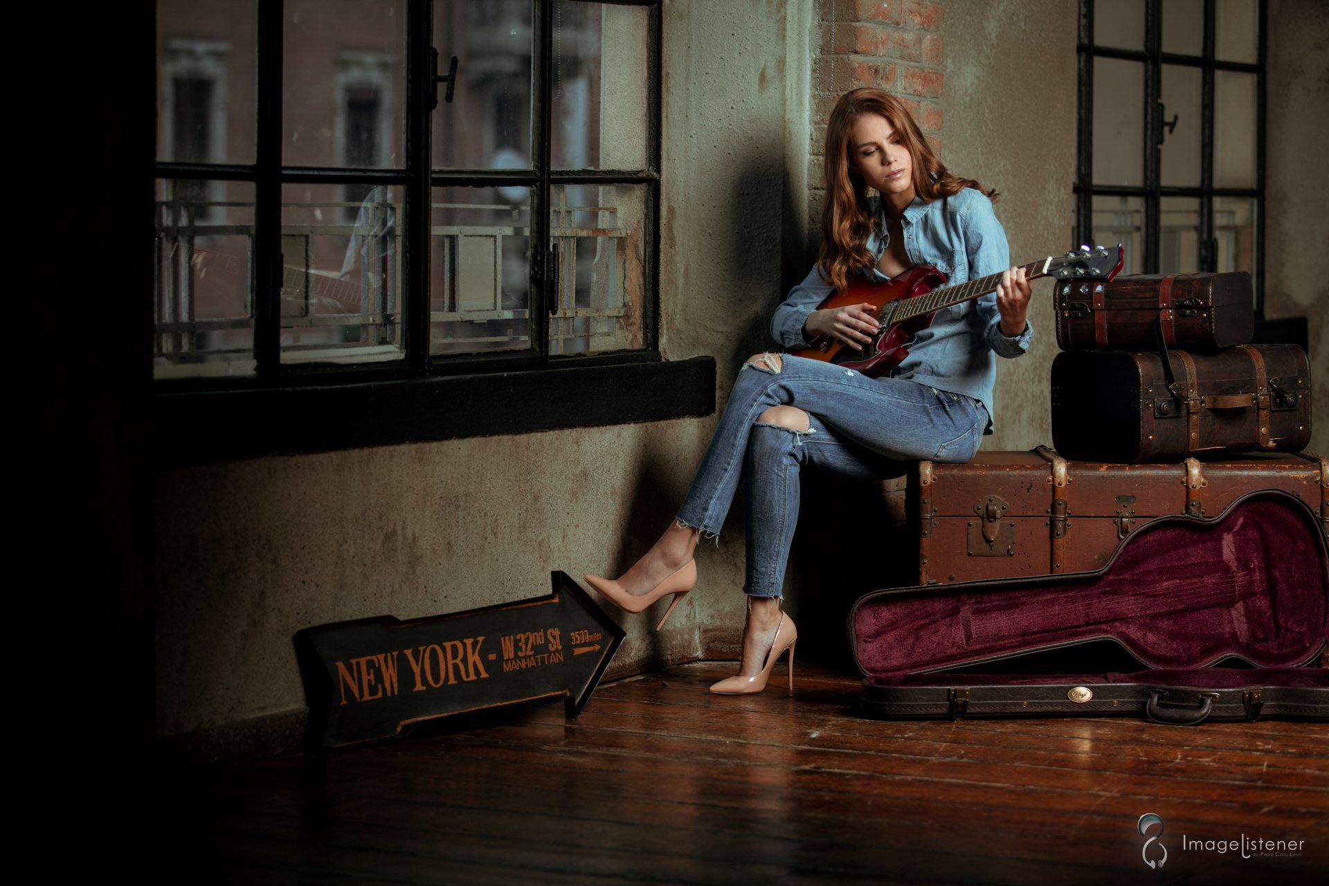 HD PC desktop wallpaper of a redheaded musician making music by loft windows, playing a guitar amid vintage suitcases and an open guitar case.
