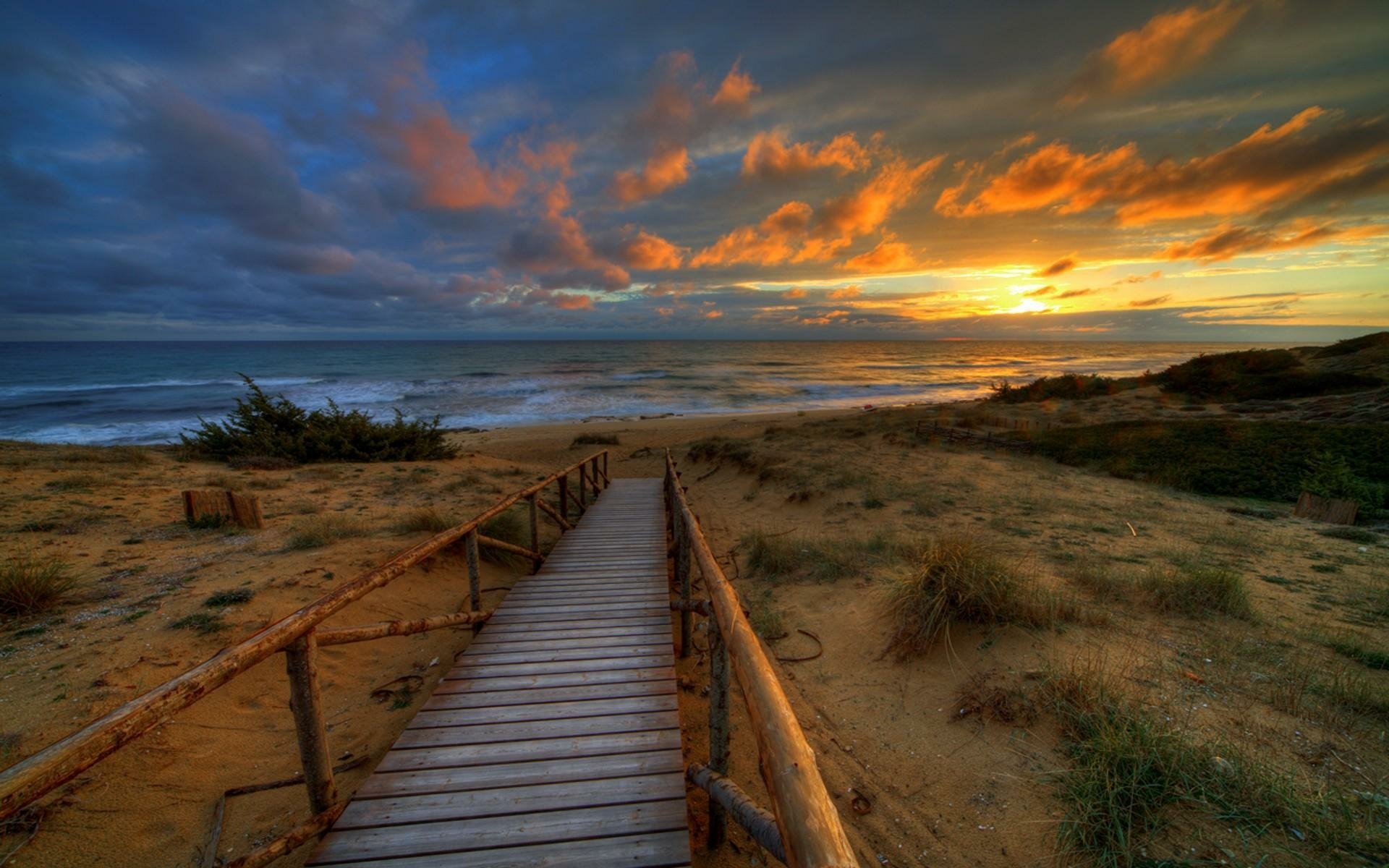 HD PC desktop wallpaper background showing a wooden walkway over sandy dunes to the ocean horizon at sunset, dramatic sky and beach landscape photography.