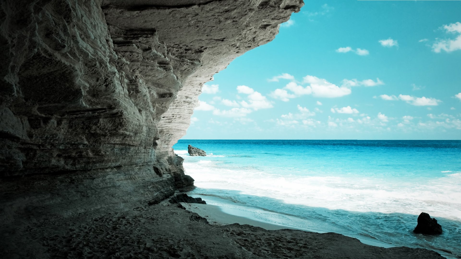 A stunning HD wallpaper depicting a serene cave by the beach, showcasing crystal-clear water and a vibrant sky, inviting you to explore the beauty of nature.