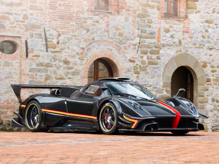 Black Pagani Zonda R supercar parked before a stone building; aggressive body, red racing stripe and accents, large rear wing — HD PC desktop wallpaper background.