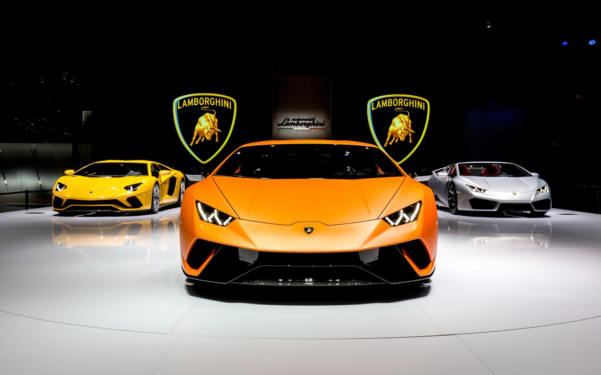 HD desktop wallpaper featuring three Lamborghini supercars prominently displayed, with the Lamborghini Huracan Performante in the center, surrounded by glowing Lamborghini logos in the background.