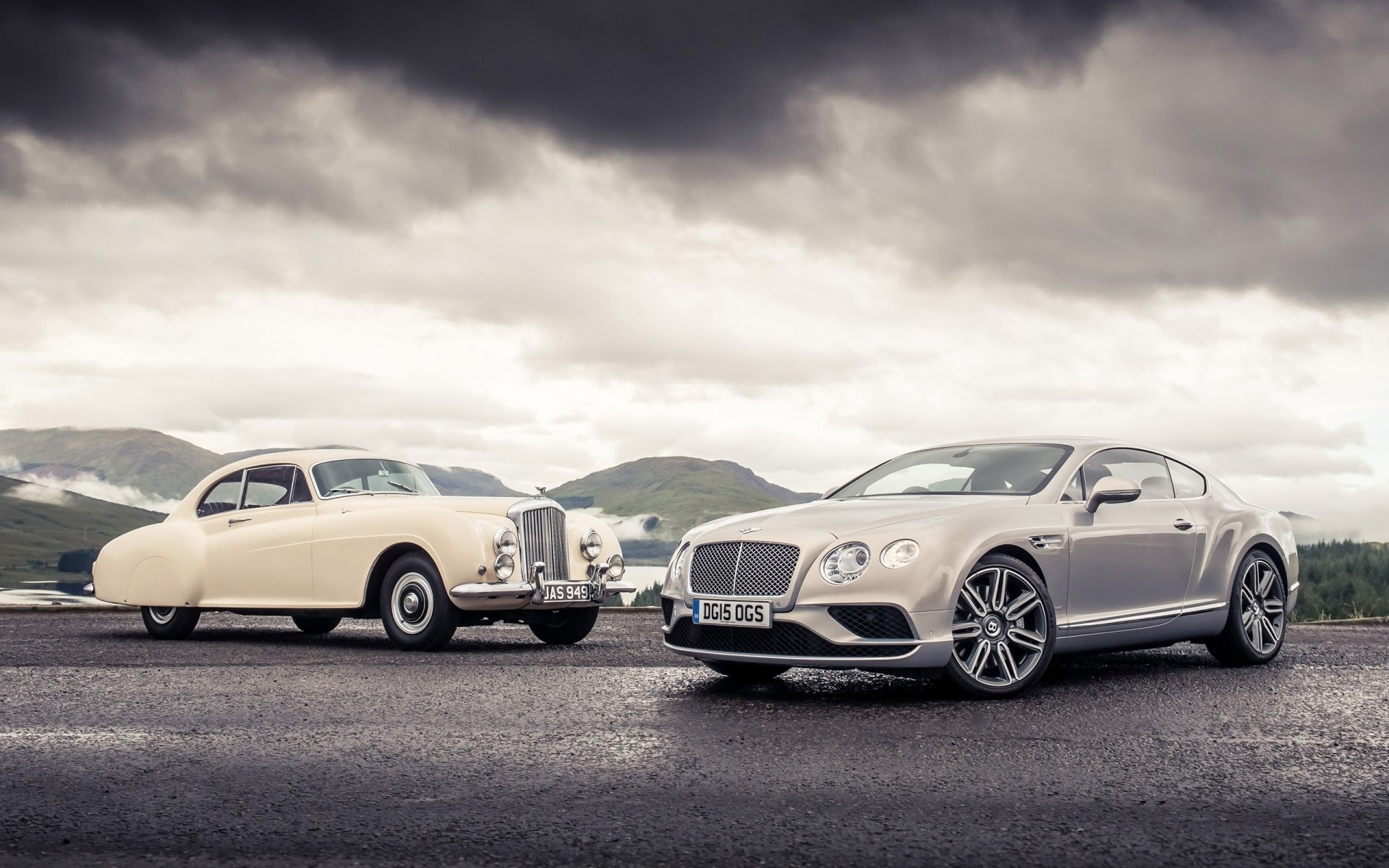 2K Quad HD PC desktop wallpaper: vintage cream Bentley Continental R‑Type and silver modern Bentley Continental parked on wet road beneath dramatic cloudy sky.