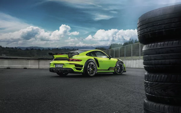 Lime green Porsche 911 Turbo S GTStreet R supercar parked on a racetrack pit lane with dramatic clouds and stacked tires in foreground — 2K Quad HD PC desktop wallpaper background.