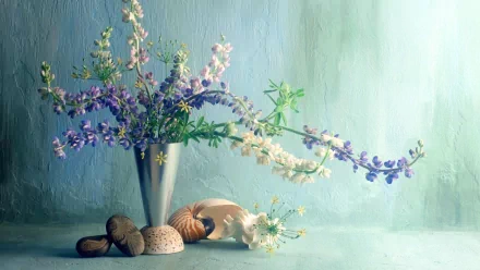 A beautifully arranged vase of colorful flowers sits among pebbles and shells, set against a soft, textured background, creating an artistic and serene desktop wallpaper.