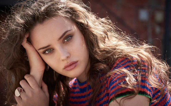 HD desktop wallpaper featuring Australian actress Katherine Langford. The brunette celebrity with blue eyes poses thoughtfully, wearing a striped shirt.