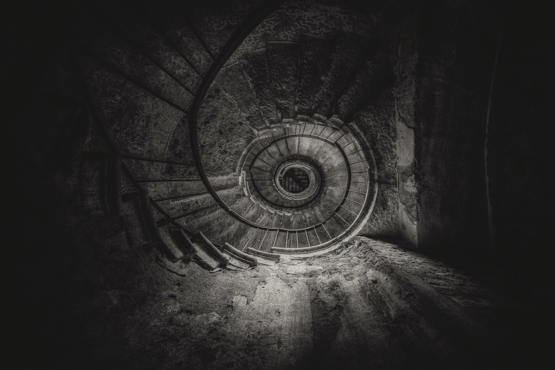 Black and white 4K Ultra HD image of a man-made spiral staircase viewed from above, highlighting the intricate curvature and textured stairs in dramatic light and shadow.