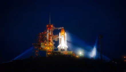 NASA's Space Shuttle Atlantis on the Cape Canaveral launch pad at night, brightly lit against a deep blue sky — 5K Ultra HD PC desktop wallpaper.