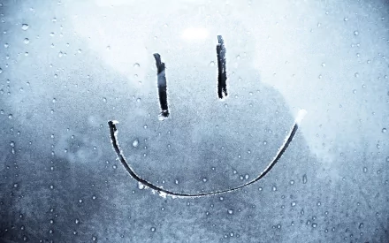 A whimsical smiley face drawn on a foggy glass surface, surrounded by droplets, serves as a charming and humorous HD desktop wallpaper and background.