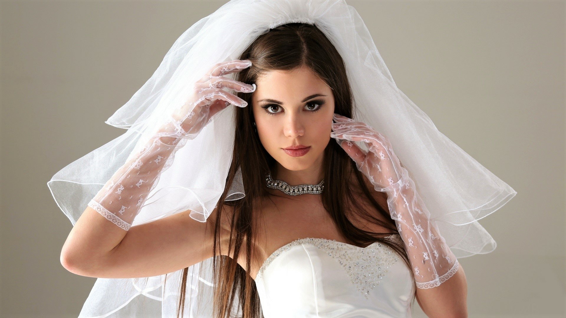 HD desktop wallpaper of a brunette bride in a white wedding dress and veil, brown-eyed woman wearing sheer embroidered gloves and a necklace.