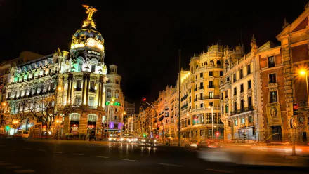 A vibrant evening cityscape of Madrid, Spain, showcasing illuminated historic buildings and architectural details under the night sky.