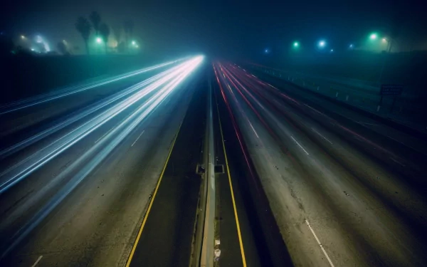 A time-lapse photograph captures blurred traffic on a highway at night, showcasing vibrant light trails against a hazy background, creating a dynamic HD wallpaper.
