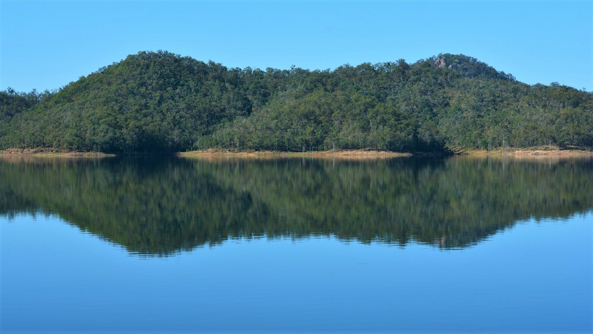Calm lake in Queensland, Australia, reflecting a lush green mountain and bay under a clear blue sky, captured in HD as a serene nature desktop wallpaper.