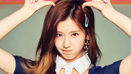HD desktop wallpaper featuring a member of the music group TWICE with a playful expression, wearing a navy outfit and blue hairclip, hands positioned on her head.