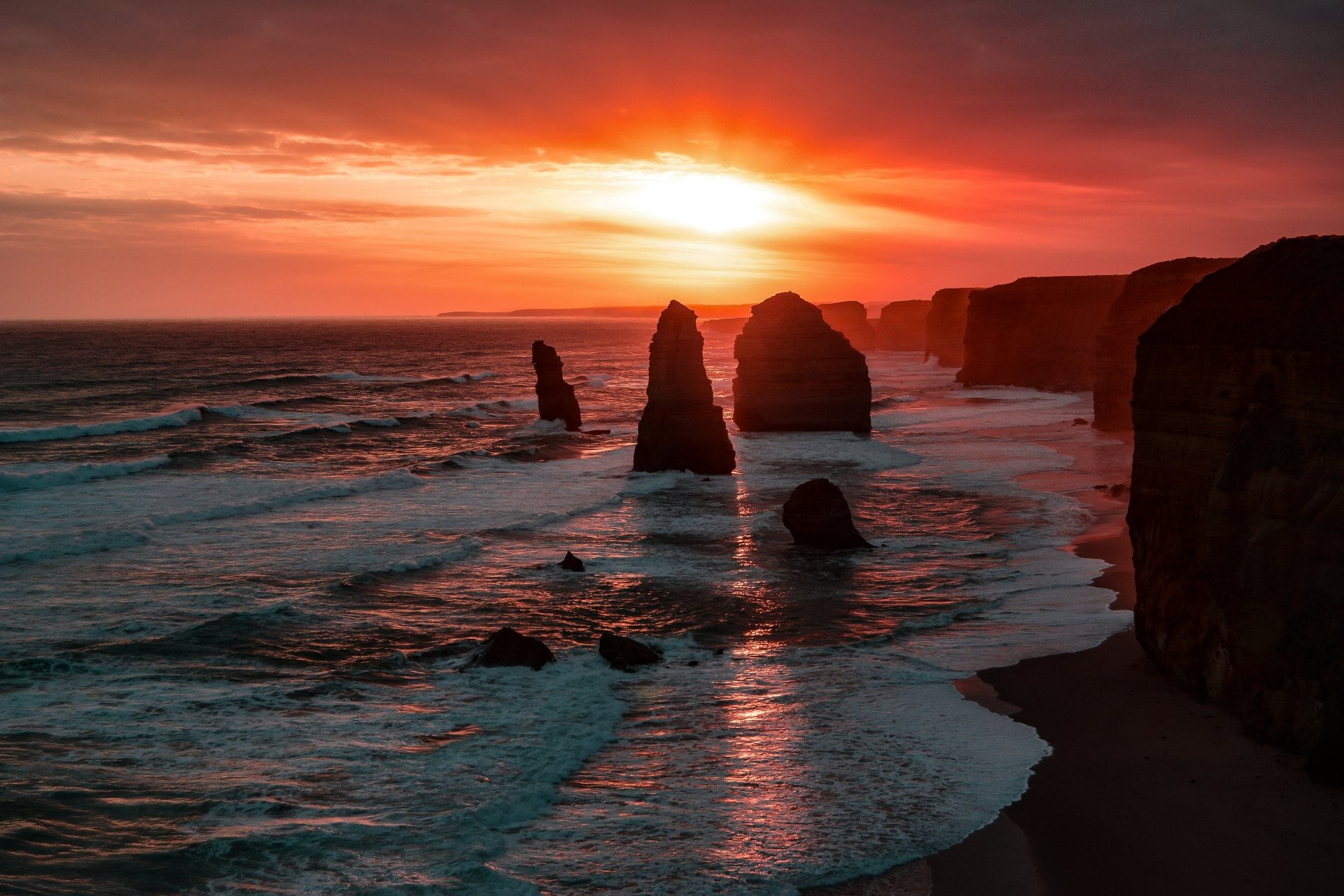 Stunning sunset over the Twelve Apostles along Australia's coastline, with vibrant skies, ocean waves, and prominent cliffs. This HD image captures the tranquil beauty of nature.