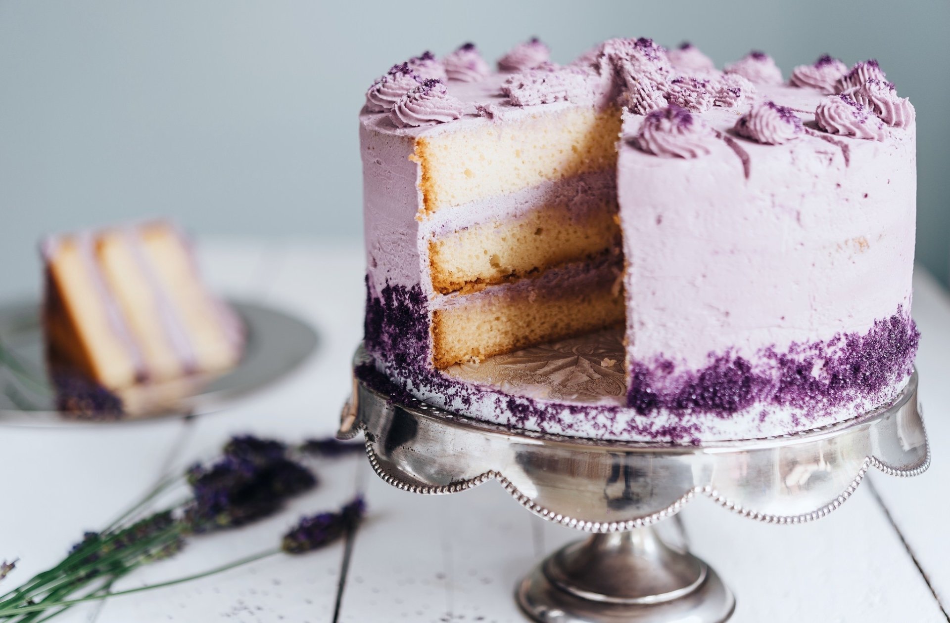A creamy purple layered cake with decorative frosting sits on a silver cake stand, showcased in an HD PC desktop wallpaper featuring a delicate pastry and food theme.