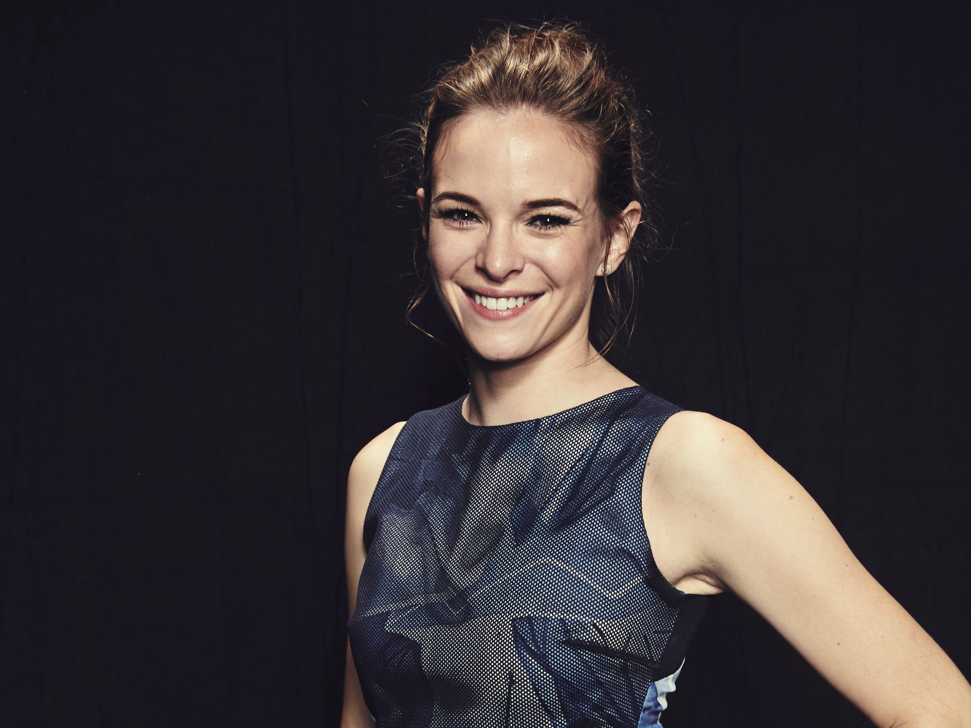 Smiling woman with hair pulled back in a sleeveless patterned dress against a dark background — 2K Quad HD PC desktop wallpaper.