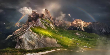 HD desktop wallpaper showing a mountain peak with scattered houses, surrounded by clouds, fog, and a vibrant rainbow arching across the natural landscape.