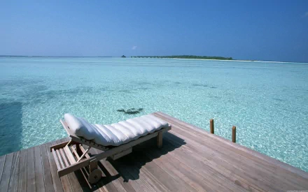 A tranquil dock extends over clear turquoise waters, featuring a comfortable lounge chair, surrounded by the serenity of the ocean under a bright blue sky—an inspiring HD wallpaper.