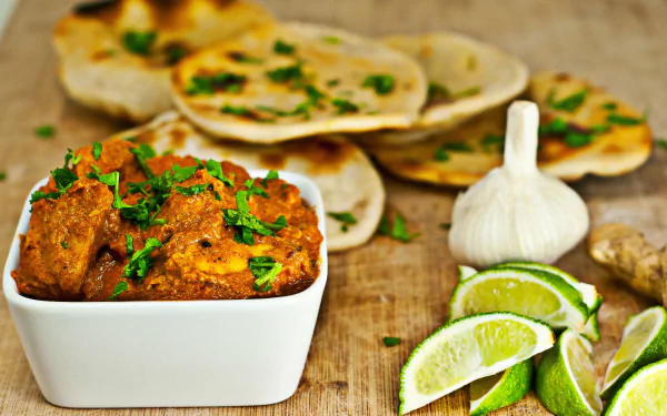 2K Quad HD desktop wallpaper of curry: white bowl of spiced curry garnished with cilantro, lime wedges, garlic and stacked flatbreads on a wooden board — meal, food, lime, Curry.