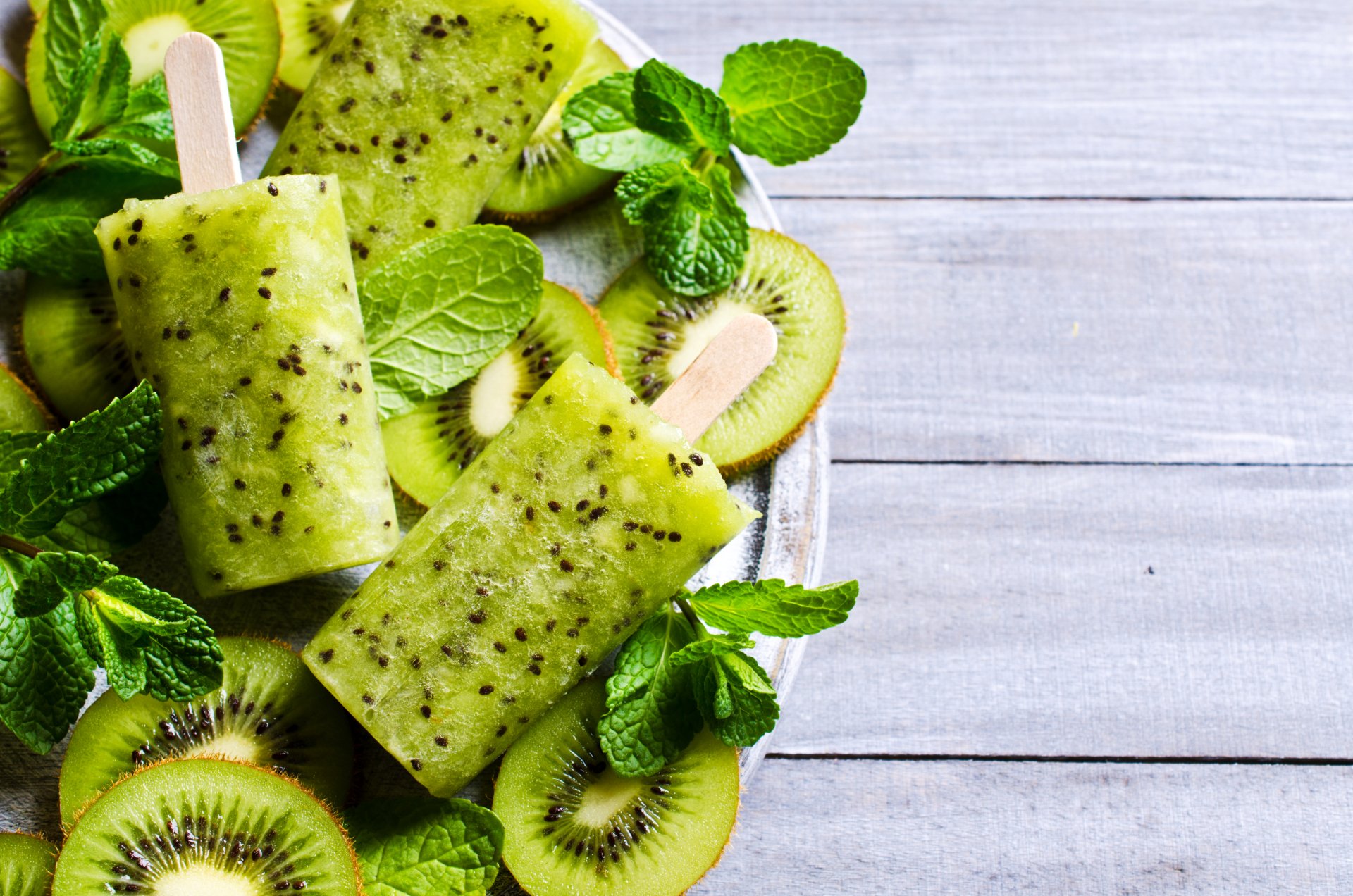 Close-up 4K Ultra HD image of kiwi fruit popsicles surrounded by fresh kiwi slices and mint leaves, creating a refreshing and vibrant ice cream scene.