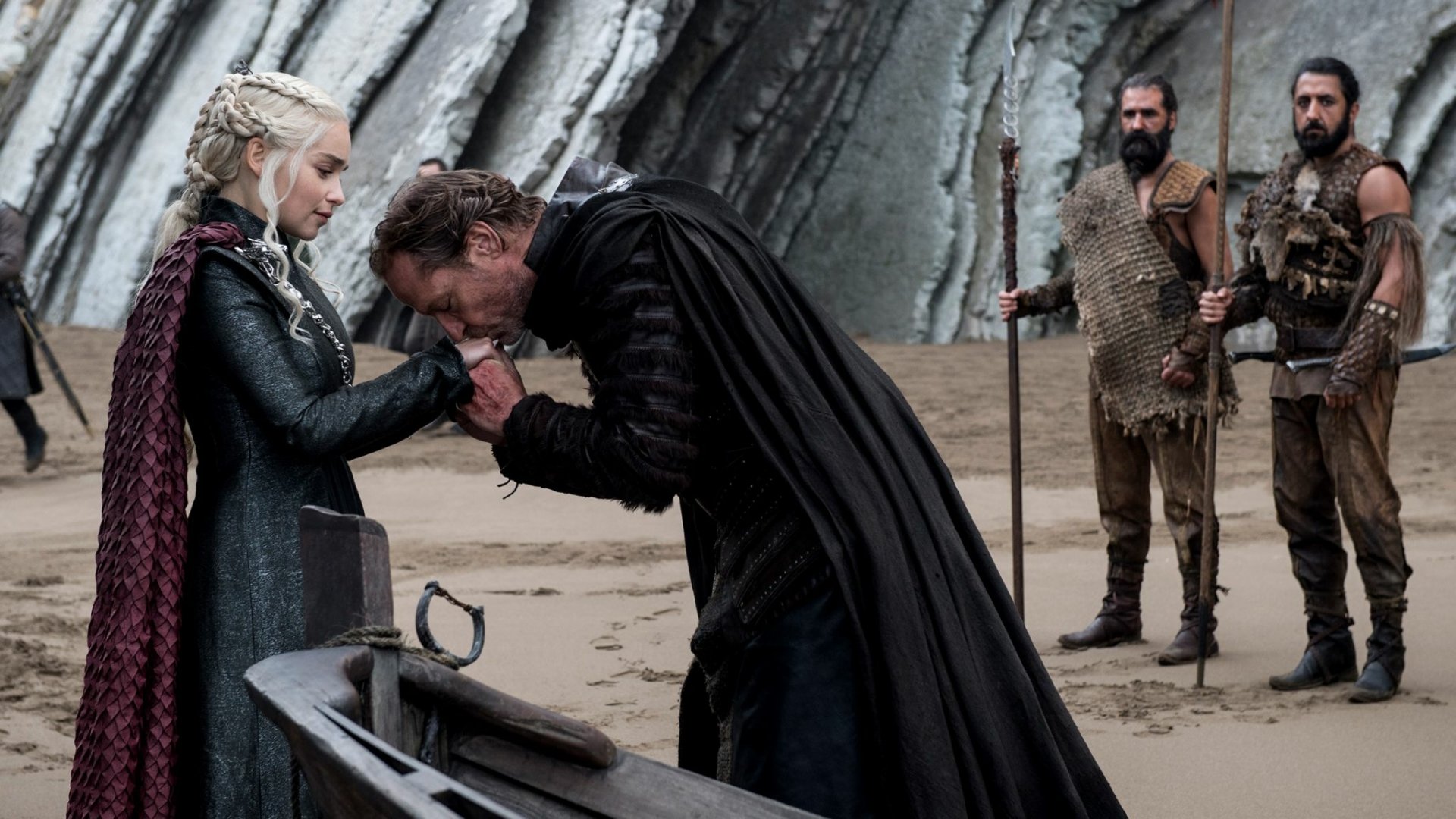 HD PC desktop wallpaper: Scene from TV show Game of Thrones — Jorah Mormont kneels and kisses Daenerys Targaryen’s hand on a windswept beach as guards stand behind.