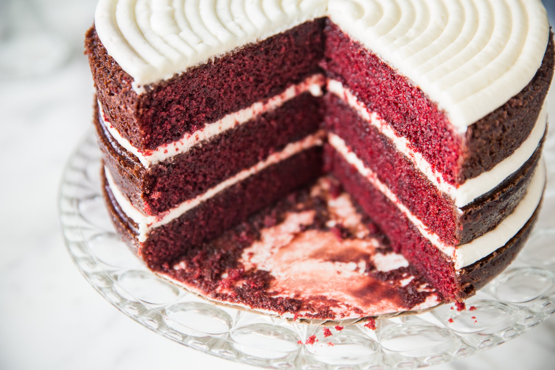 HD PC desktop wallpaper background: close-up pastry/food image of a sliced red velvet cake with white cream cheese frosting swirls on a glass cake stand.