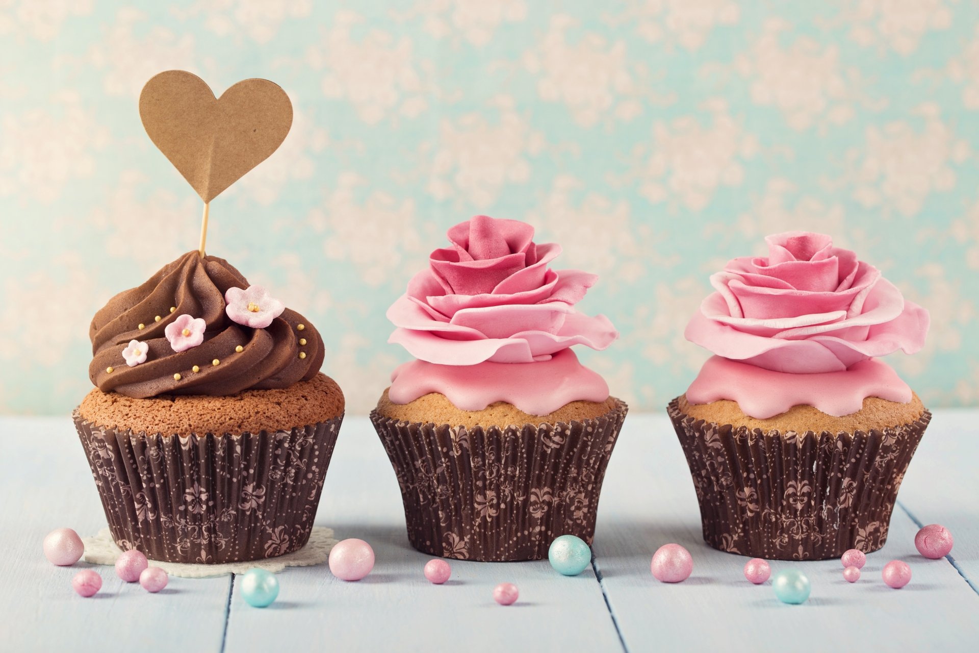 Three cupcakes with chocolate and pink cream icing decorated with small candy pearls, displayed against a pastel floral background in 4K Ultra HD resolution.