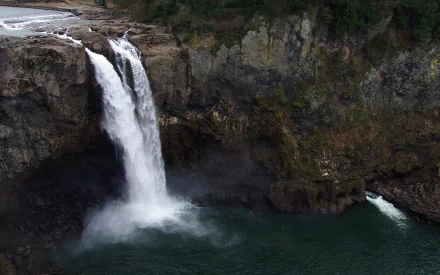 HD PC desktop wallpaper of Snoqualmie Falls: a powerful waterfall dropping into an emerald pool framed by mossy cliffs and evergreen forest.