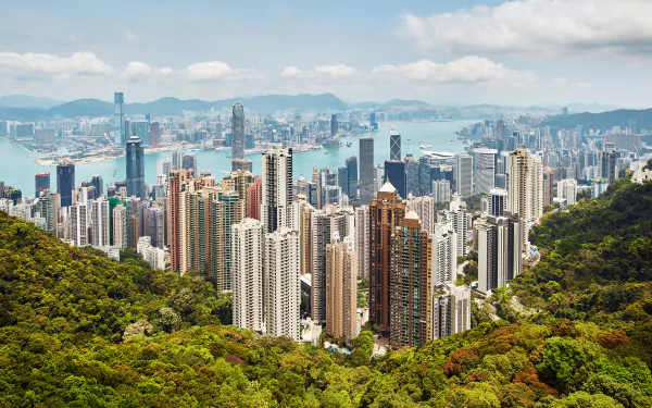 4K Ultra HD wallpaper showcasing Hong Kong's dense cityscape with towering man-made buildings nestled between lush green hills under a partly cloudy sky.
