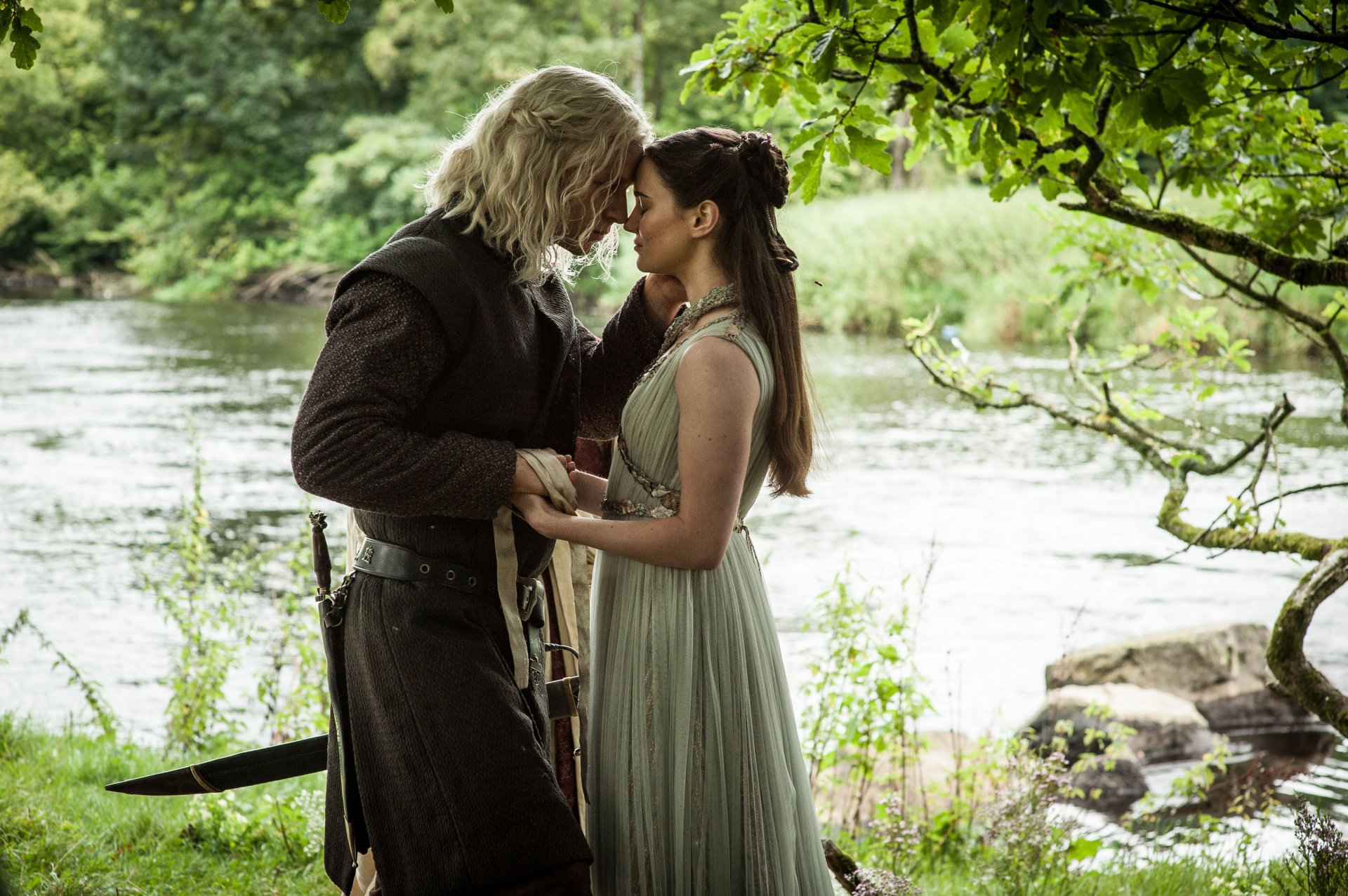 A romantic scene from the TV show Game of Thrones, featuring two characters embracing near a serene riverside, surrounded by lush greenery. 4K Ultra HD wallpaper.