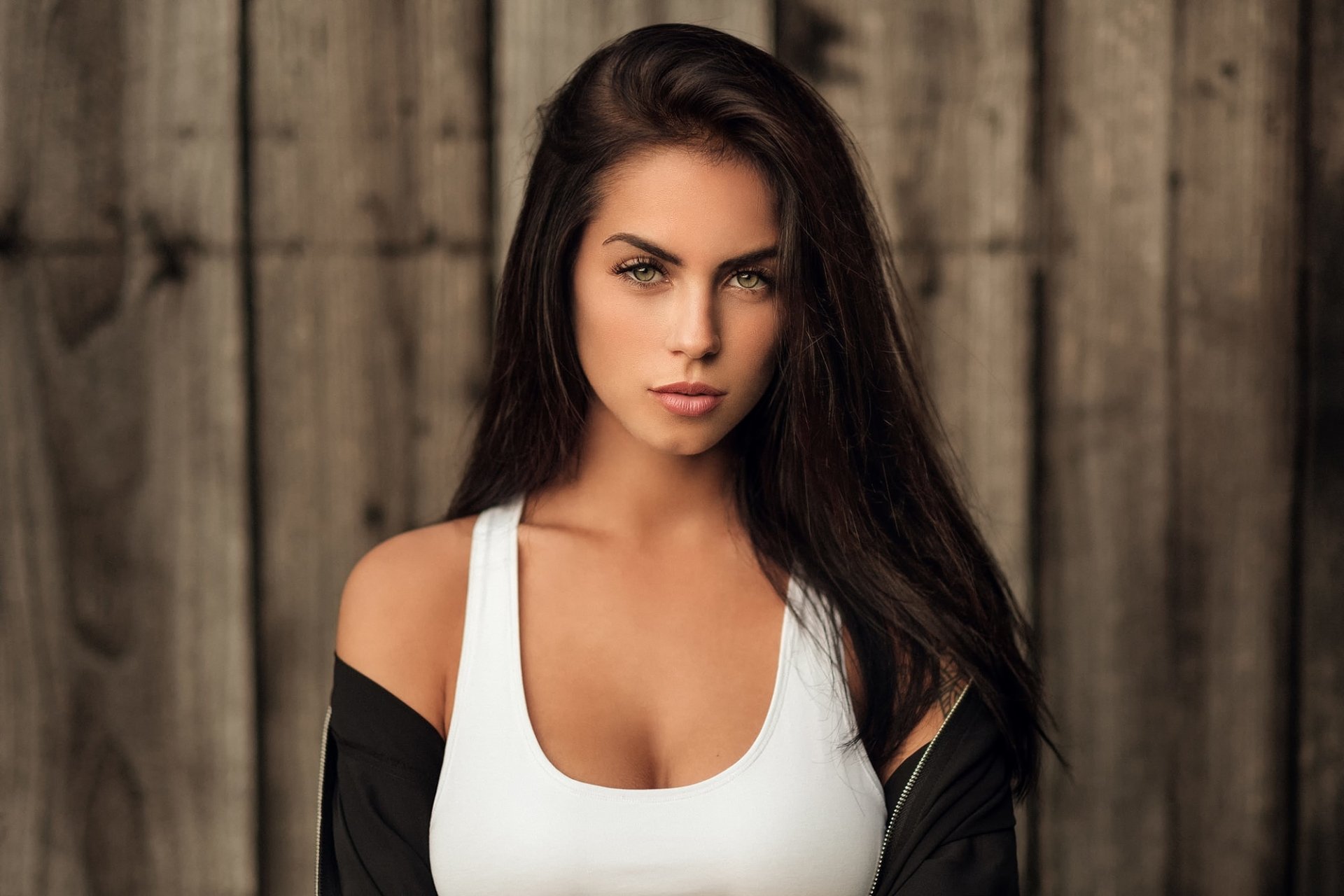 HD wallpaper of a brunette woman, posed confidently in front of a wooden background, showcasing her model features.