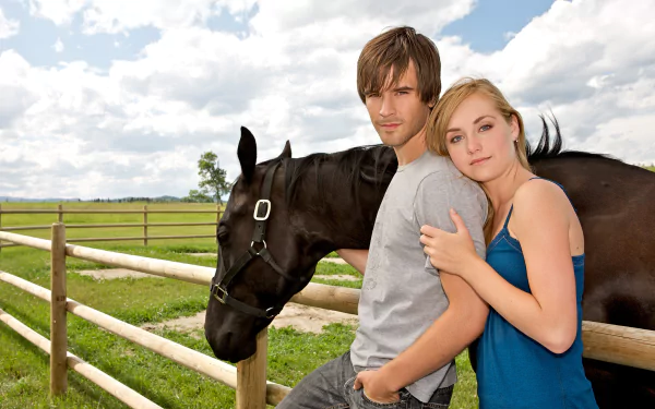 HD PC desktop wallpaper for Heartland: young man and woman leaning on a fence with a black horse in a sunlit pasture under a blue sky with clouds.