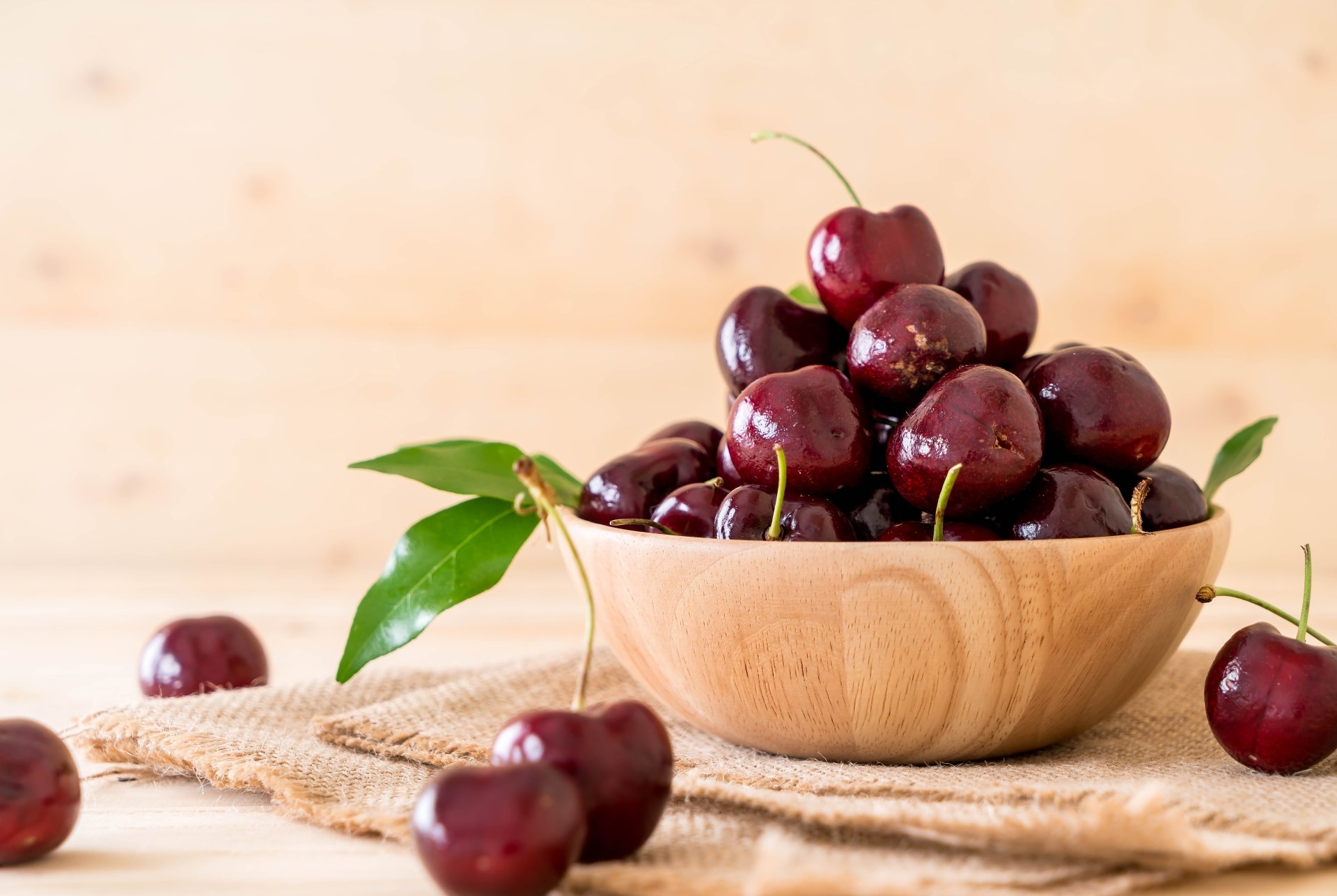 A wooden bowl filled with fresh cherries, surrounded by loose cherries and green leaves, captured in vibrant detail for an 8K Ultra HD PC desktop wallpaper.