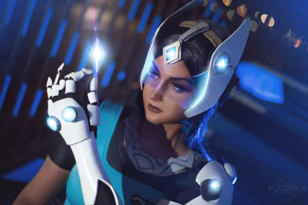 HD PC desktop wallpaper: woman cosplaying Symmetra from Overwatch, close-up with glowing headpiece and hand light construct against a blue futuristic background.
