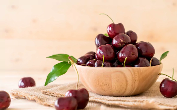 A wooden bowl filled with fresh cherries, surrounded by loose cherries and green leaves, captured in vibrant detail for an 8K Ultra HD PC desktop wallpaper.
