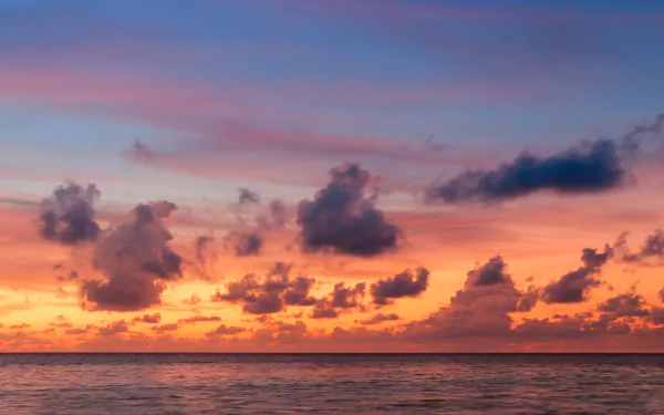 HD wallpaper of a stunning sunset over the ocean, with vibrant clouds scattered across the colorful sky, blending from deep orange to soft pink and blue at the horizon.