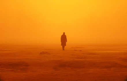 HD desktop wallpaper of Ryan Gosling in a scene from the movie Blade Runner 2049, featuring a solitary figure walking into a hazy, orange-hued landscape.